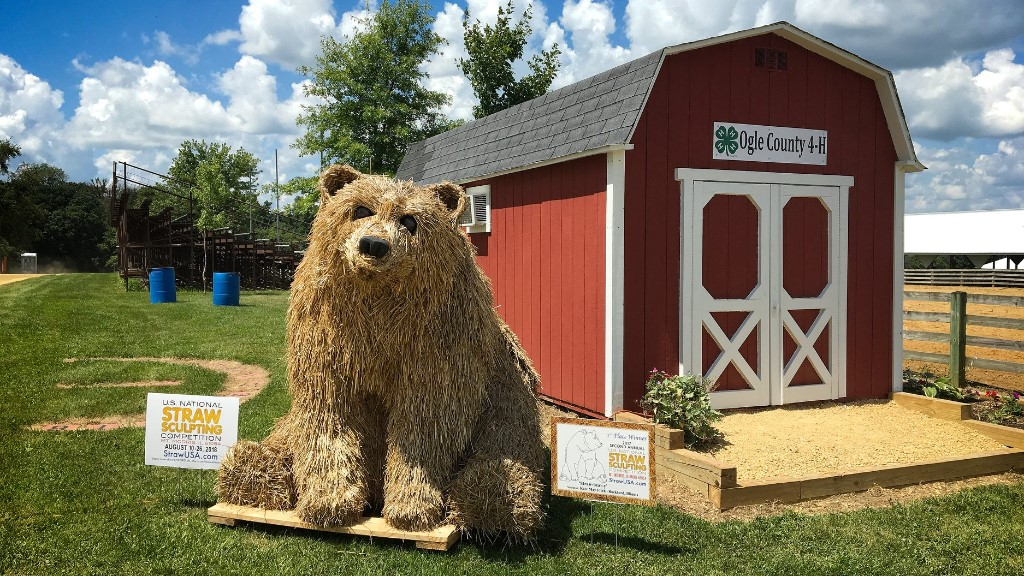 Straw sculpture of a bear placed in front of a red barn