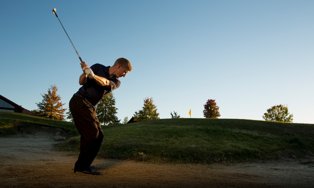 Man swinging golf club on course